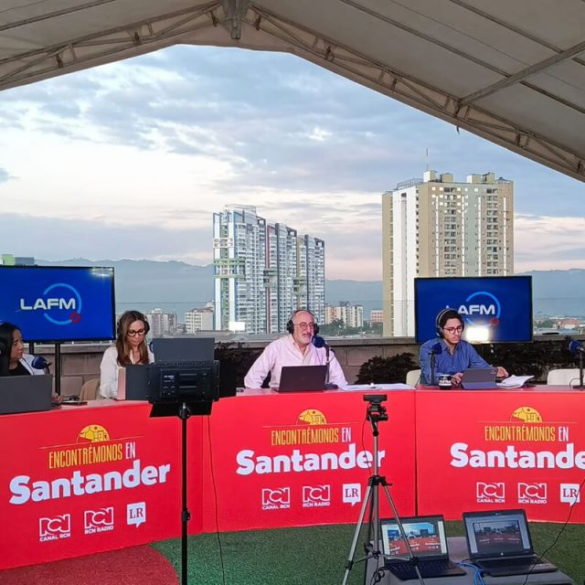 Transmisión en vivo del programa “Encontrémonos en Santander” desde una terraza con vista a edificios de la ciudad, con varios locutores trabajando frente a micrófonos y computadores