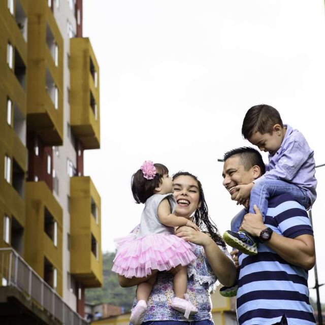 Una fotografía de una familia sonriendo. En el fondo se encuentran apartamentos