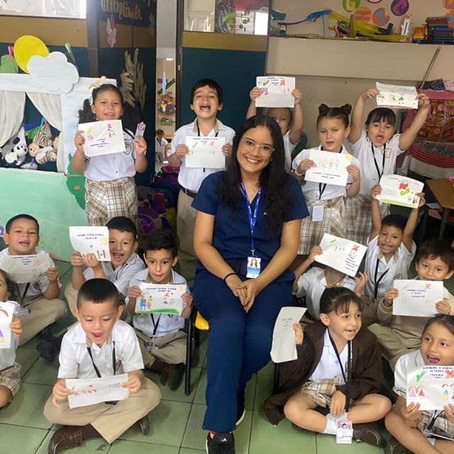 Grupo de niños de preescolar en un aula de Cajasan mostrando dibujos hechos por ellos, acompañados por su docente sentada al centro. El ambiente es colorido, alegre y decorado con materiales educativos