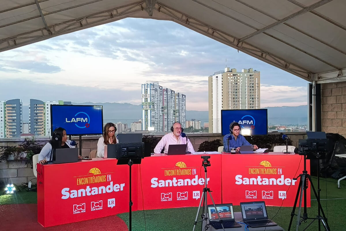 Transmisión en vivo del programa “Encontrémonos en Santander” desde una terraza con vista a edificios de la ciudad, con varios locutores trabajando frente a micrófonos y computadores