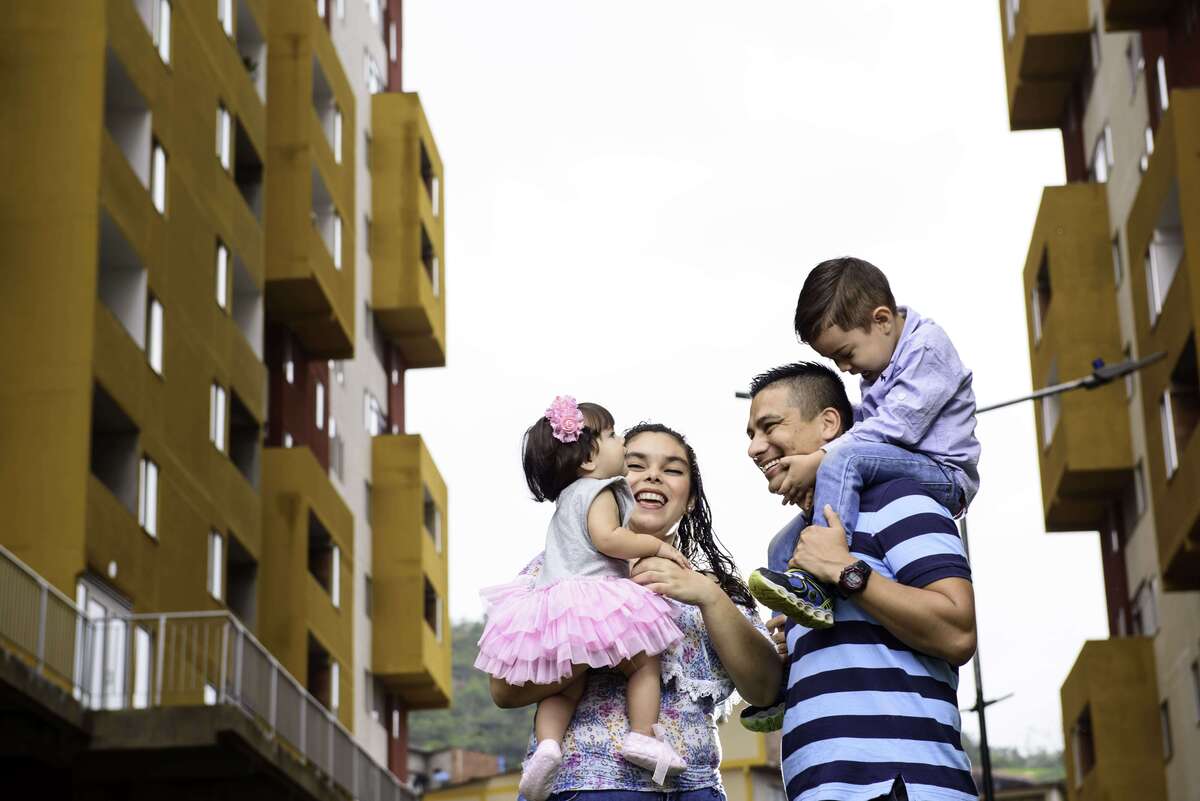 Una fotografía de una familia sonriendo. En el fondo se encuentran apartamentos
