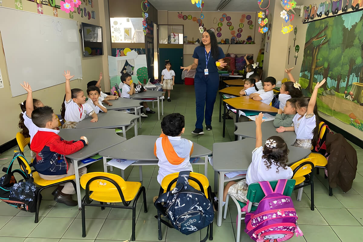 Docente guiando una actividad participativa con niños de preescolar en un aula de Cajasan, mientras varios estudiantes levantan la mano para intervenir