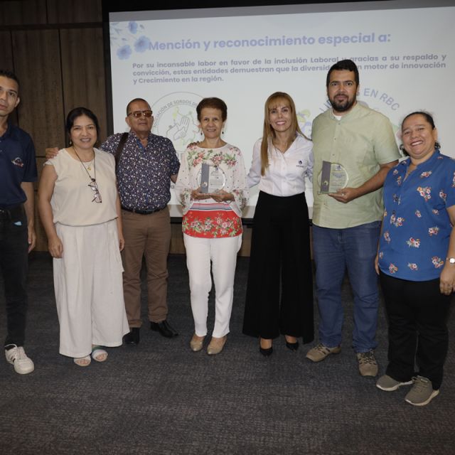 Grupo de personas posando durante una ceremonia de reconocimiento a entidades por su labor en inclusión laboral, con dos de los participantes sosteniendo trofeos frente a una pantalla con la mención especial de Cajasan