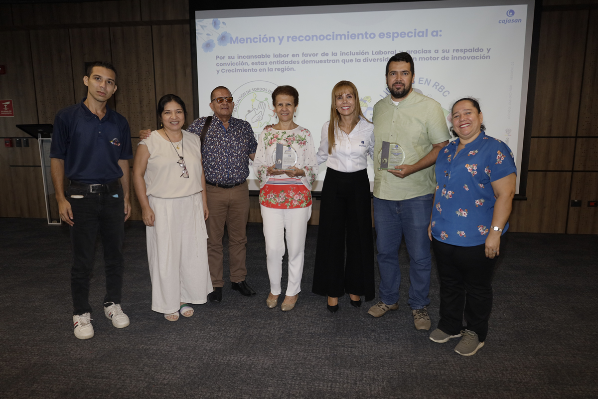 Grupo de personas posando durante una ceremonia de reconocimiento a entidades por su labor en inclusión laboral, con dos de los participantes sosteniendo trofeos frente a una pantalla con la mención especial de Cajasan