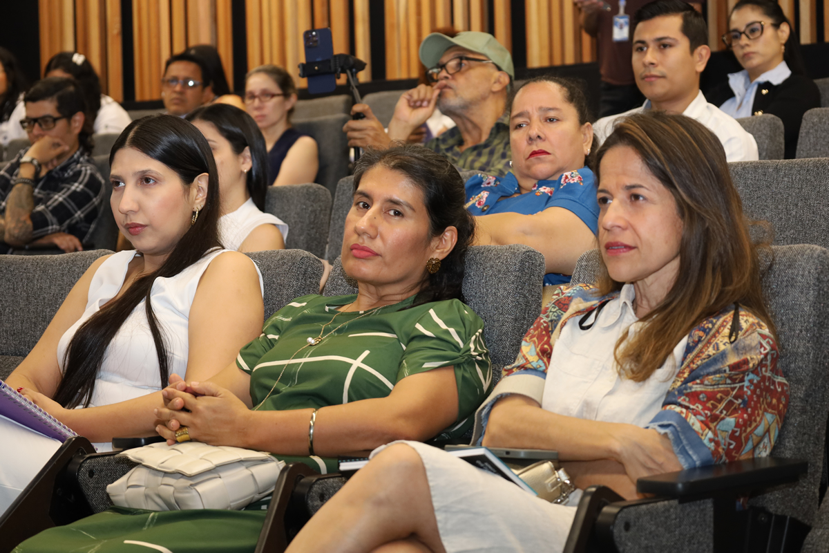 Personas sentadas en un auditorio atendiendo una conferencia o presentación, observando con atención al expositor