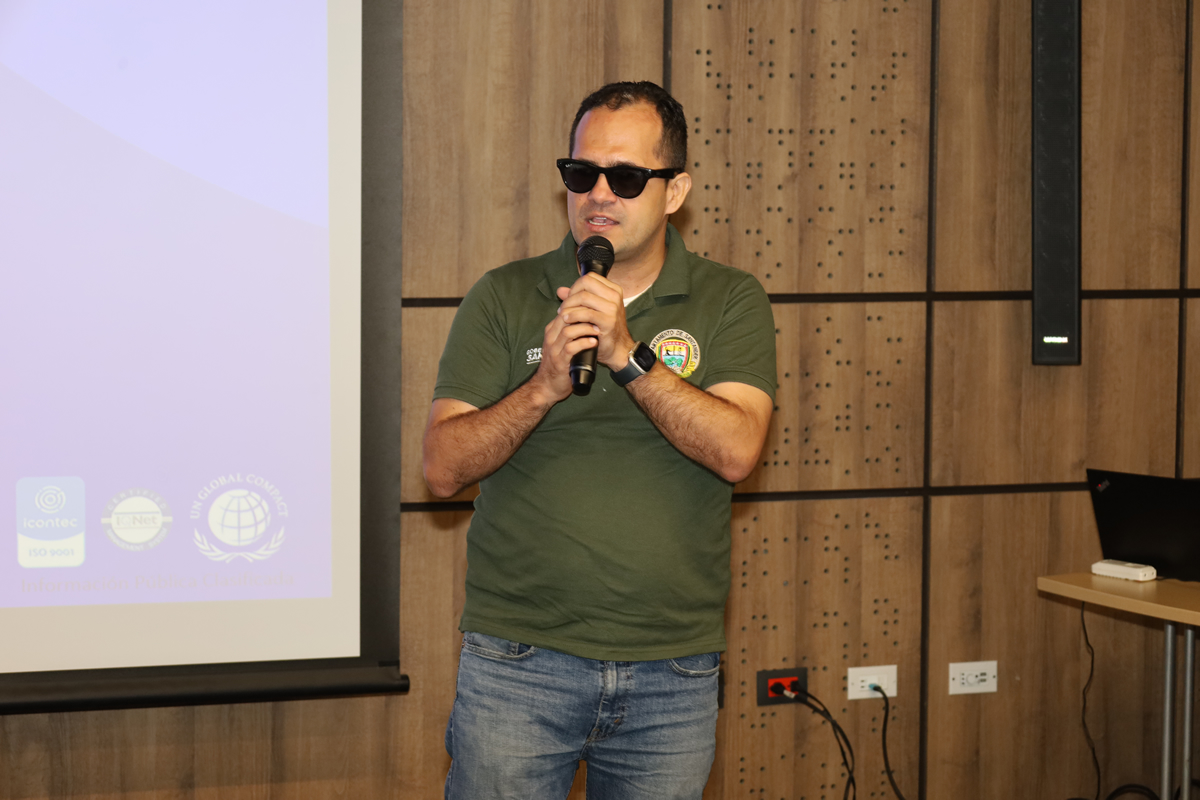 ersona de pie hablando al micrófono durante una presentación en un evento institucional