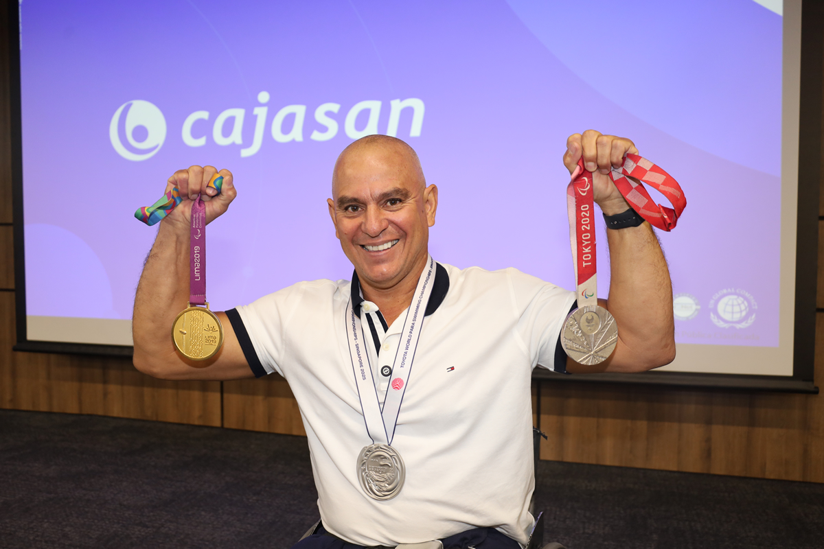 Persona sonriendo y mostrando varias medallas deportivas frente a una pantalla con el logo de Cajasan