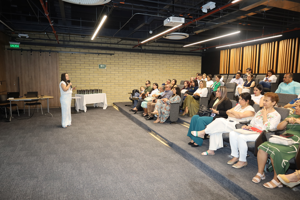 Persona de pie hablando al micrófono frente a un auditorio lleno de asistentes durante un evento institucional.