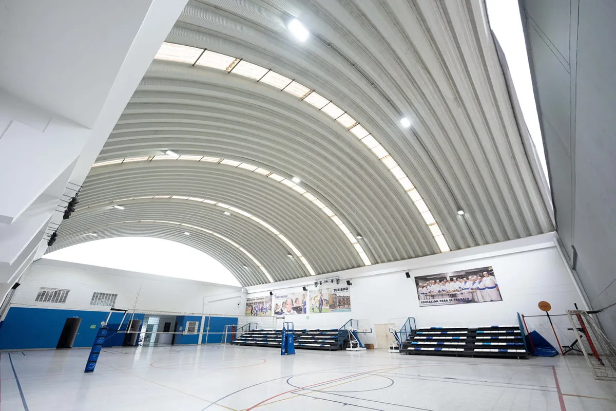 Cancha cubierta multiusos con piso de madera, gradas laterales y redes de voleibol