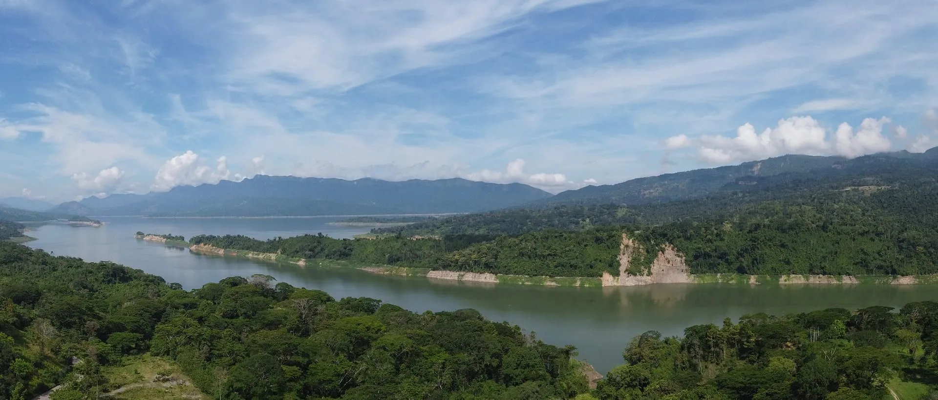 Vista panorámica del embalse Topocorrodeado por exuberante vegetación y montañas al fondo, bajo un cielo parcialmente despejado.